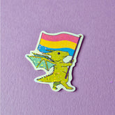 A sticker that has a cute dragon carrying a pansexual pride flag. This pride sticker makes a great gift