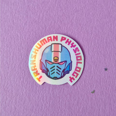 A holographic finish sticker that reads 'Transhuman physiology'. Featuring a 40k helmet in trans colours.