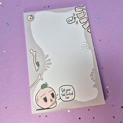 Memo pad with decorative border showing various skeleton and skulls. Top right has a spine that is cracking with 'Ow!' speech bubble coming from it. Bottom left has a skull with a small frog on it. Skull has speech buble saying 'Get your shit sorted luv,'